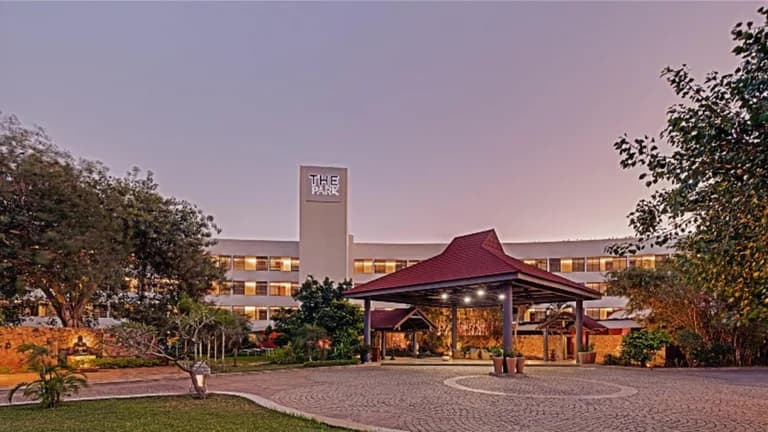 The Park Visakhapatnam hotel exterior at dusk, showing the main entrance, driveway, and lush surrounding greenery.